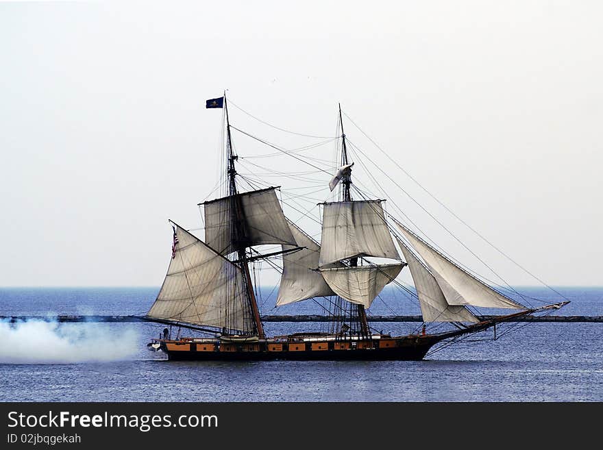 Tallship smoke firing from back, tall ship on lake Ontario's blue water and solid clouds, wind blowing, sailor wearing orange rain pants. You can almost feel the hot hazy heat. Flag blowing that says don't give up the ship. Tallship smoke firing from back, tall ship on lake Ontario's blue water and solid clouds, wind blowing, sailor wearing orange rain pants. You can almost feel the hot hazy heat. Flag blowing that says don't give up the ship.