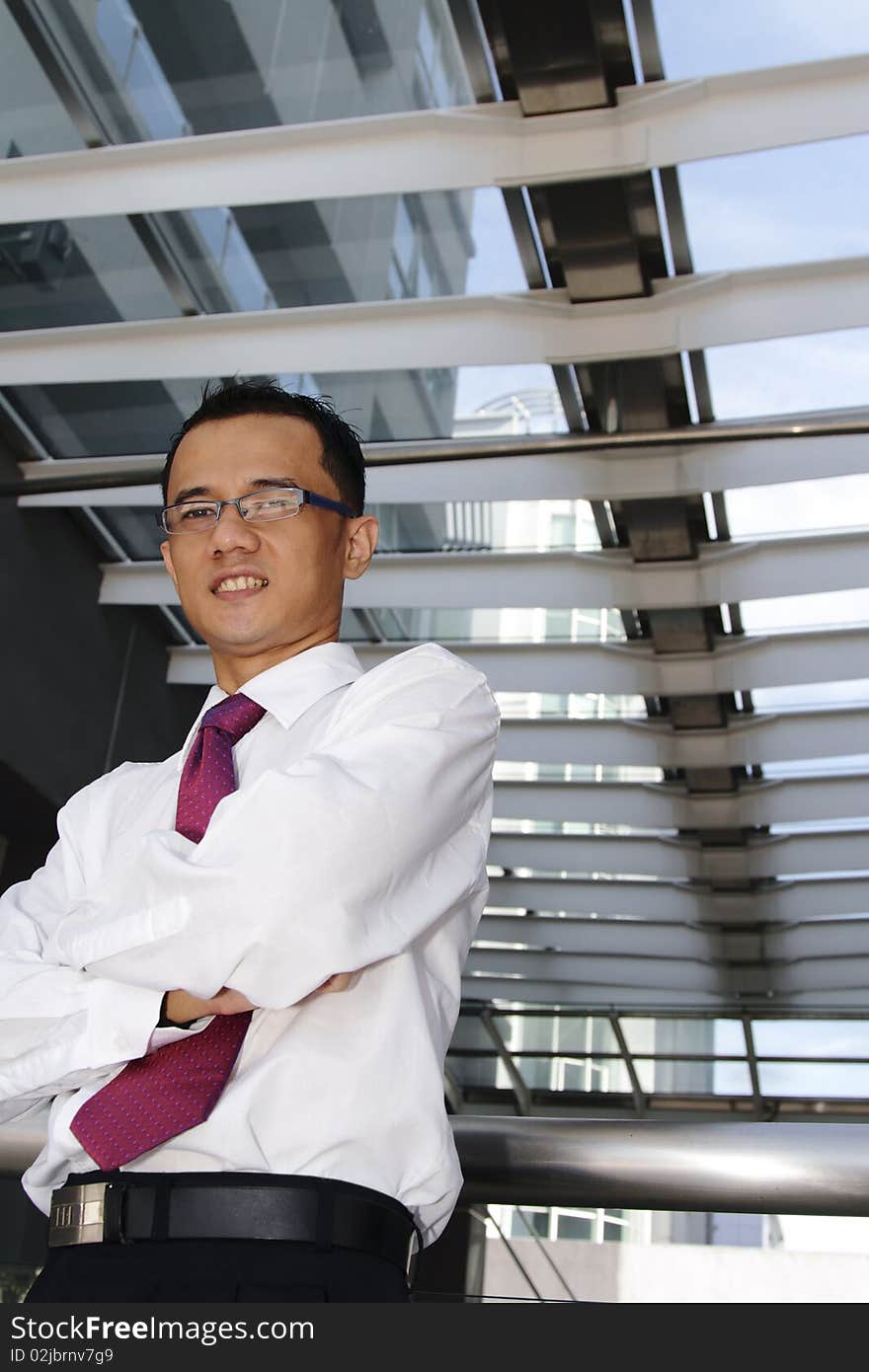 A smiling young successful Asian businessman standing with his arms crossed below a skylight