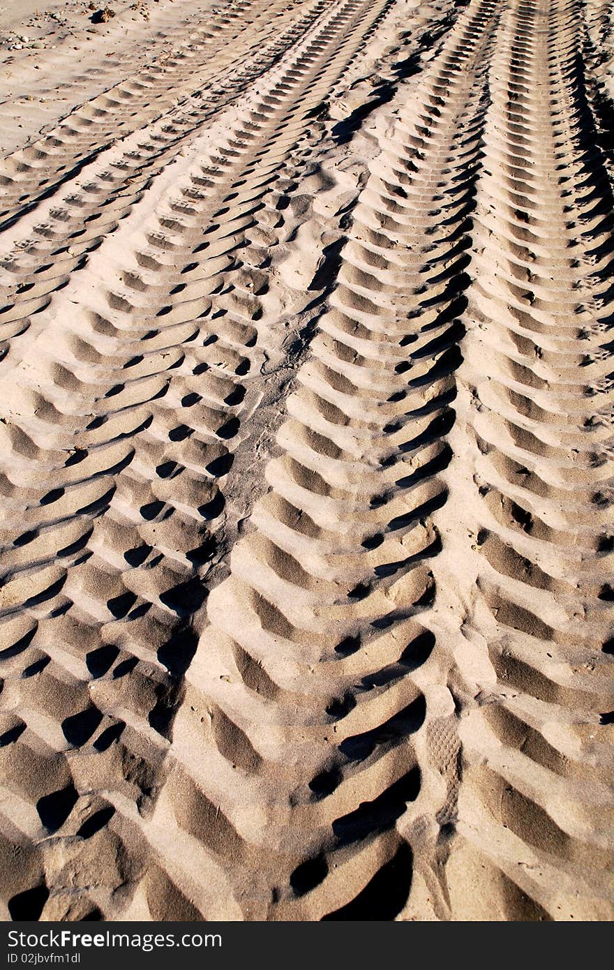 Dramatic sand tracks making a detailed texture with highlights and shadows of a large tire track in the tan sand, leading the eye into the image. Able to see several multi tan tones of natural color sand in the fresh tracks on the beach.