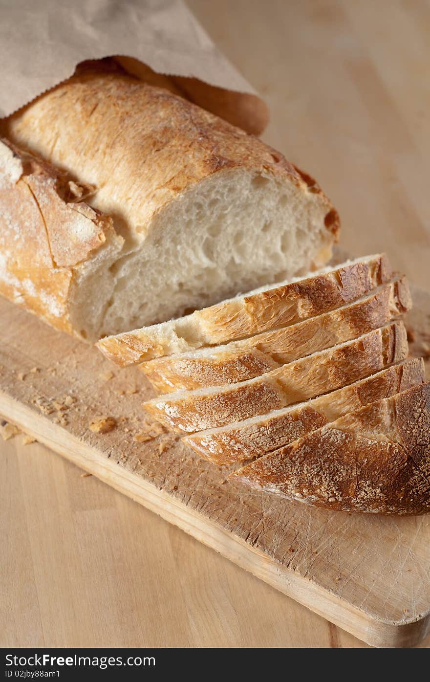 Partially Sliced Loaf of Bread on Wood Cutting Board and in brown paper bag