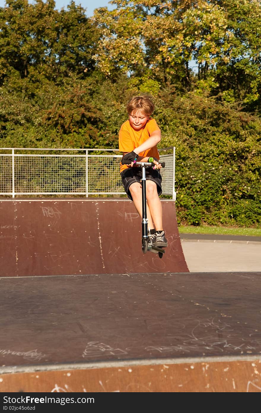 Child, boy is jumping with a scooter over a fun box in the skate parc and enjoying it. Child, boy is jumping with a scooter over a fun box in the skate parc and enjoying it