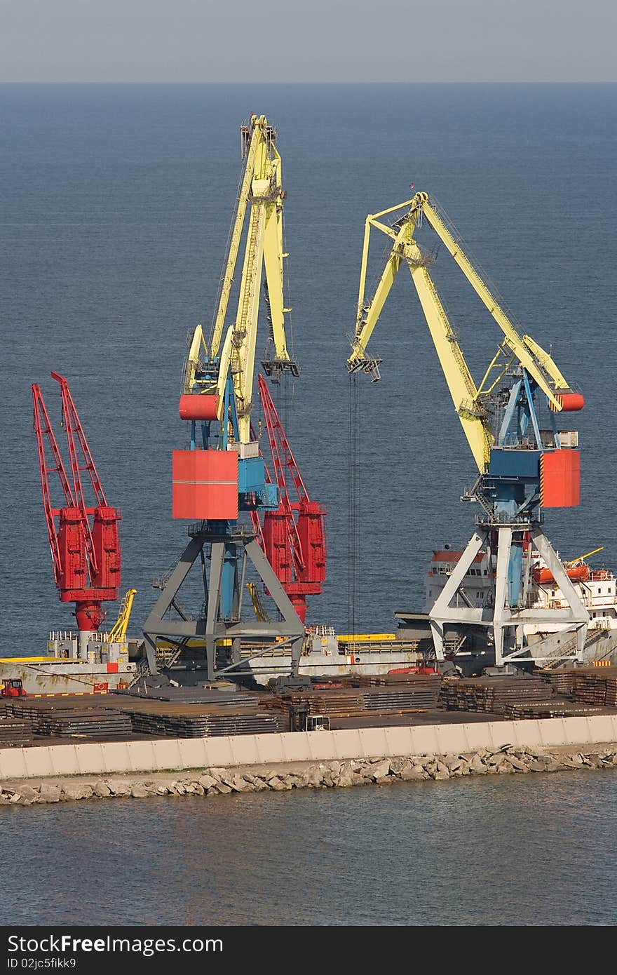 Two heavy industrial cranes working at the commercial dock in the middle of a day. Two heavy industrial cranes working at the commercial dock in the middle of a day