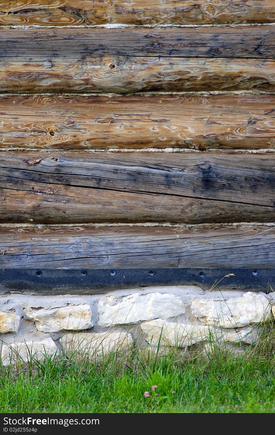 Wall of log house, stone base, lawn