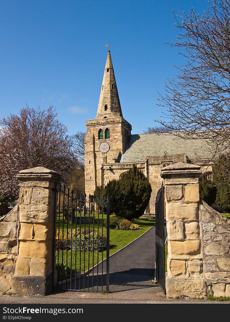 A small church with a leaning tower and spire. The gate leads the eye into the churchyard through the grounds to the church. A small church with a leaning tower and spire. The gate leads the eye into the churchyard through the grounds to the church.