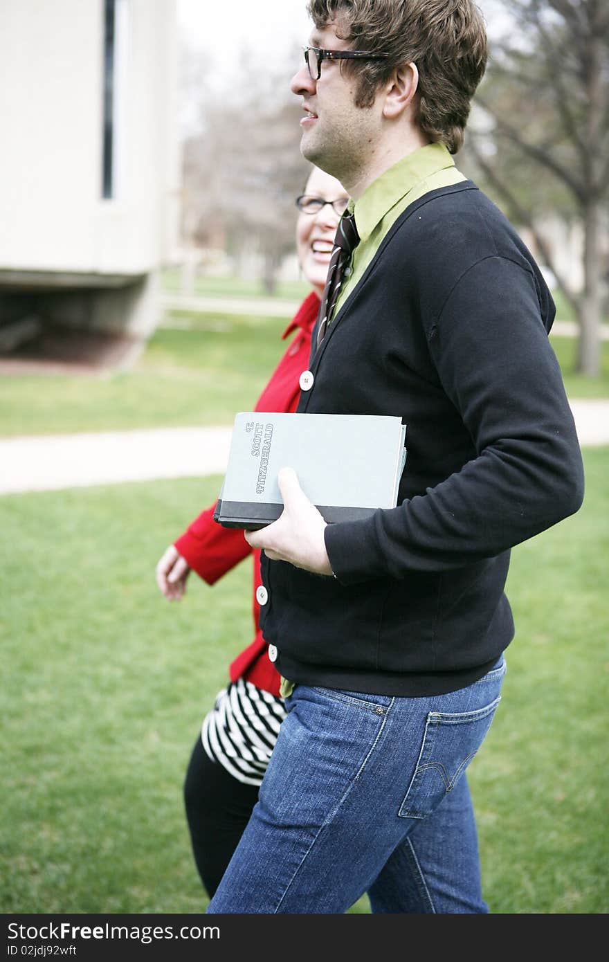 Male and female college student holding books walking on grass on campus grounds going to class. Male and female college student holding books walking on grass on campus grounds going to class