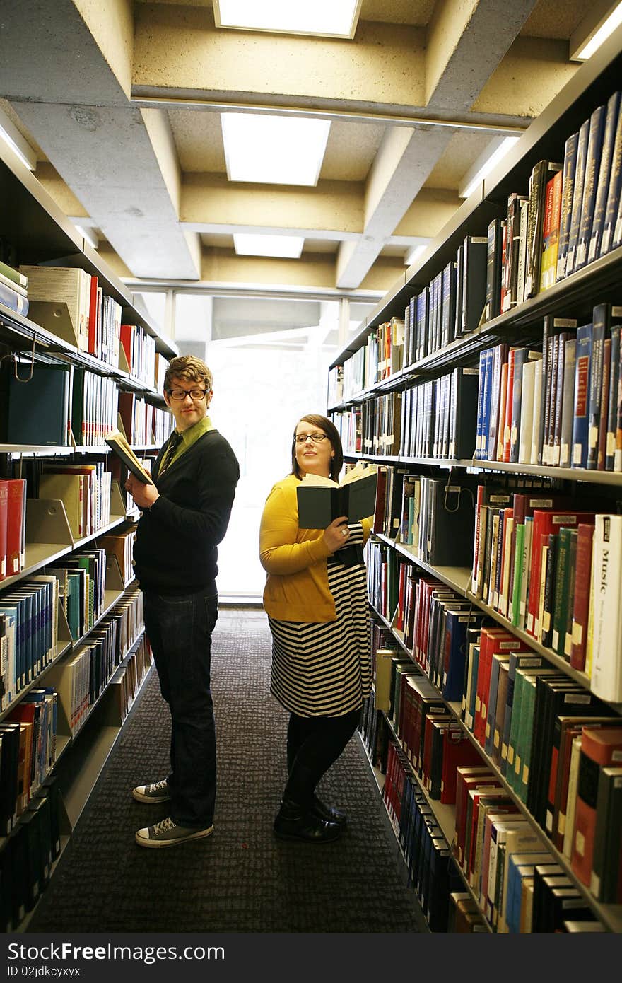 College age students reading books in library whispering to each other in library. College age students reading books in library whispering to each other in library