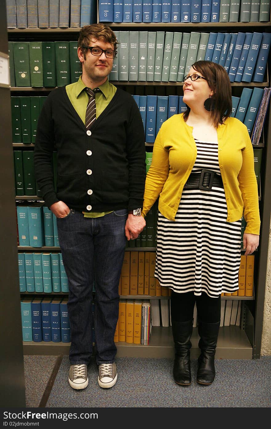 College age students holding hands standing in front of books in library. College age students holding hands standing in front of books in library