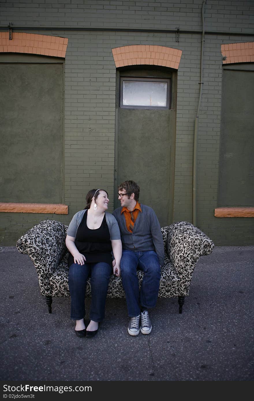 Young couple sitting together on pattern couch outside on the city street in front of building. Young couple sitting together on pattern couch outside on the city street in front of building