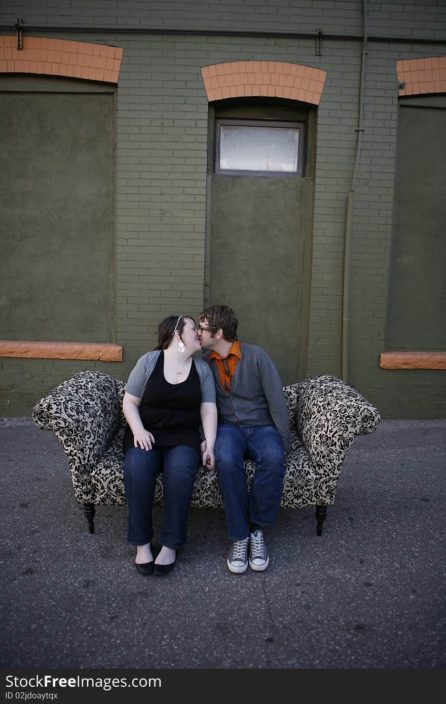 Young couple sitting together on pattern couch outside on the city street in front of building. Young couple sitting together on pattern couch outside on the city street in front of building