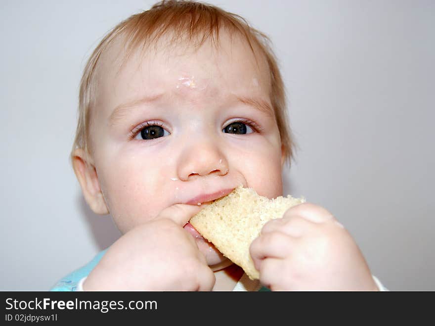 The small soiled kid has control over a piece of a white loaf and bites off it. The small soiled kid has control over a piece of a white loaf and bites off it