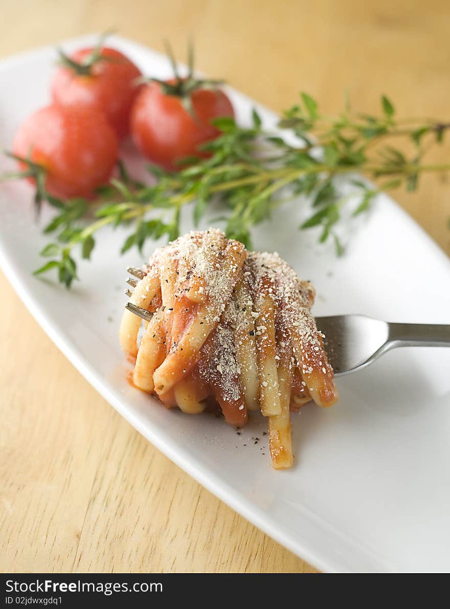 Linguine in tomato sauce and parmesan, coiled around fork on tasting plate with fresh herbs and cherry tomatos in background. Linguine in tomato sauce and parmesan, coiled around fork on tasting plate with fresh herbs and cherry tomatos in background.