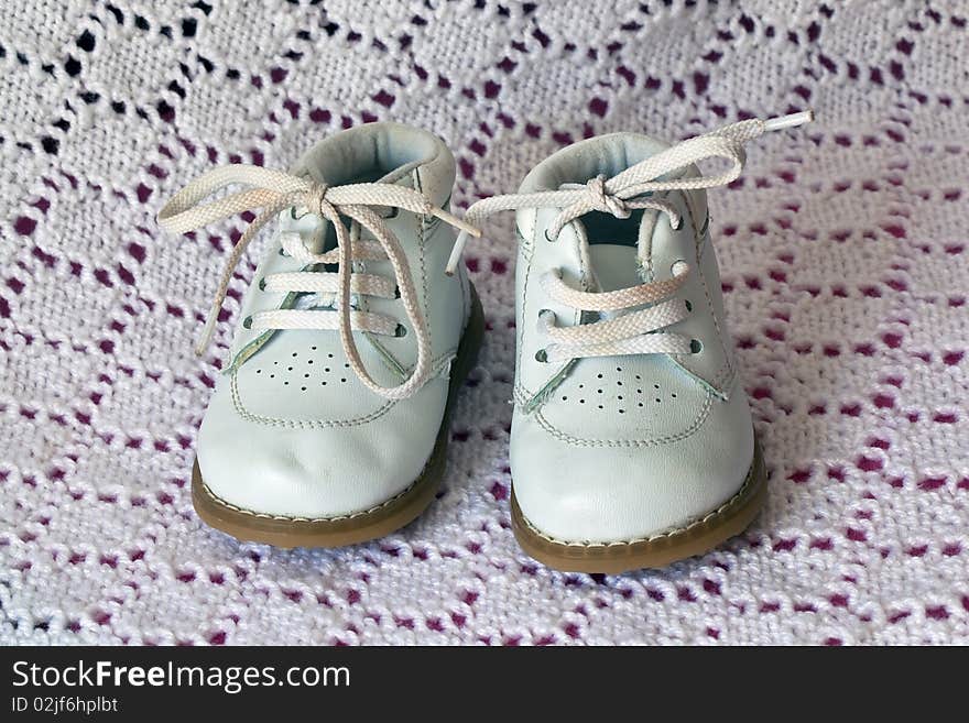 White leather baby shoes on a baby white crochet blanket background