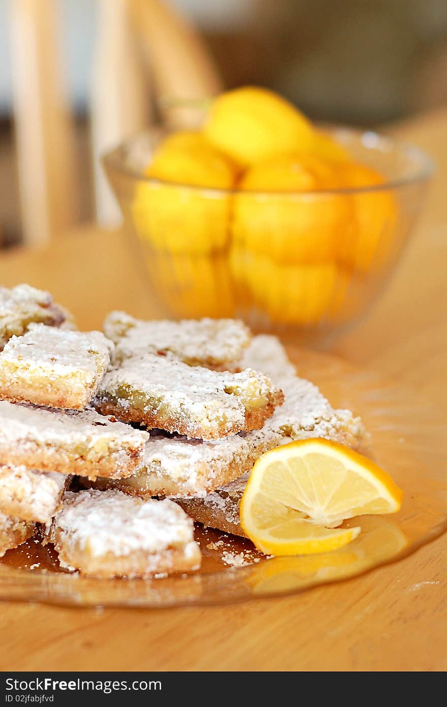 Plate of Powdered Sugar Dusted Lemon Shortbread Bars on Kitchen Table with Bowl of Lemons in Background