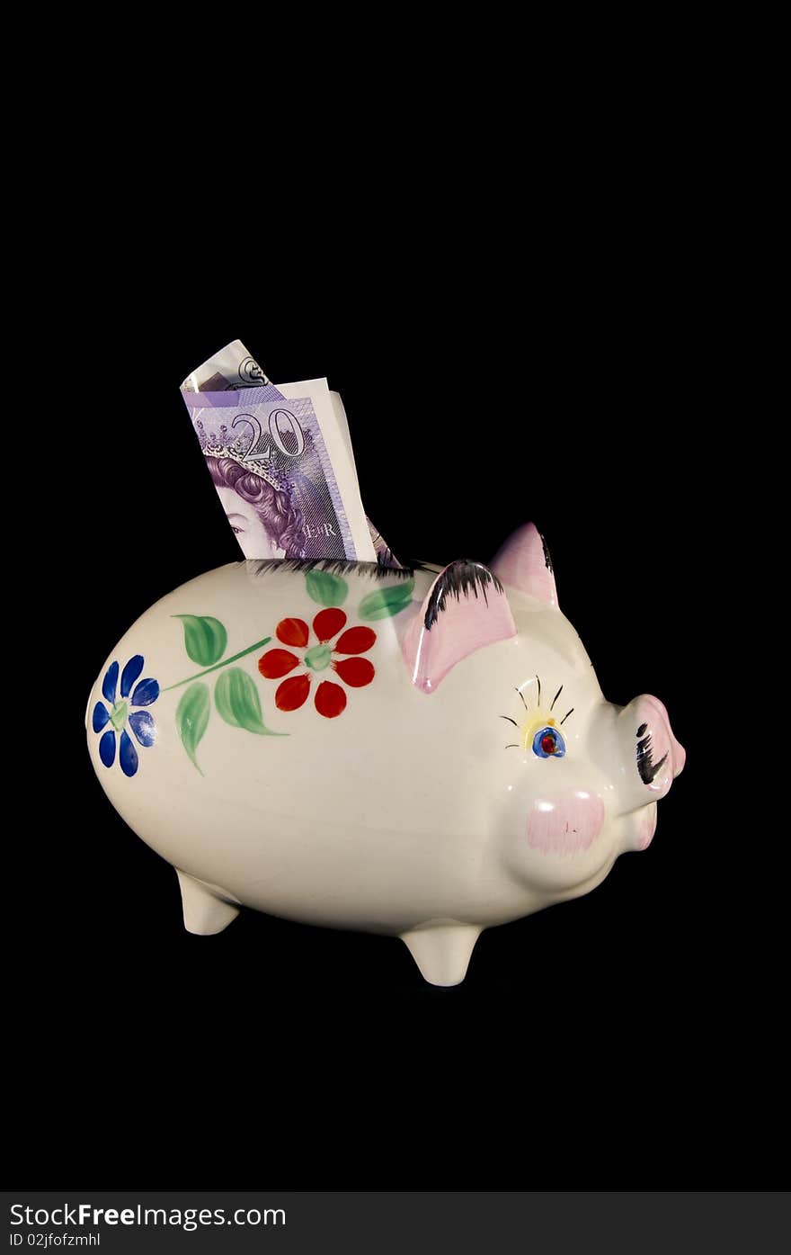 Old china piggy bank with flower pattern and money in the slot on a black background in portrait format. Old china piggy bank with flower pattern and money in the slot on a black background in portrait format