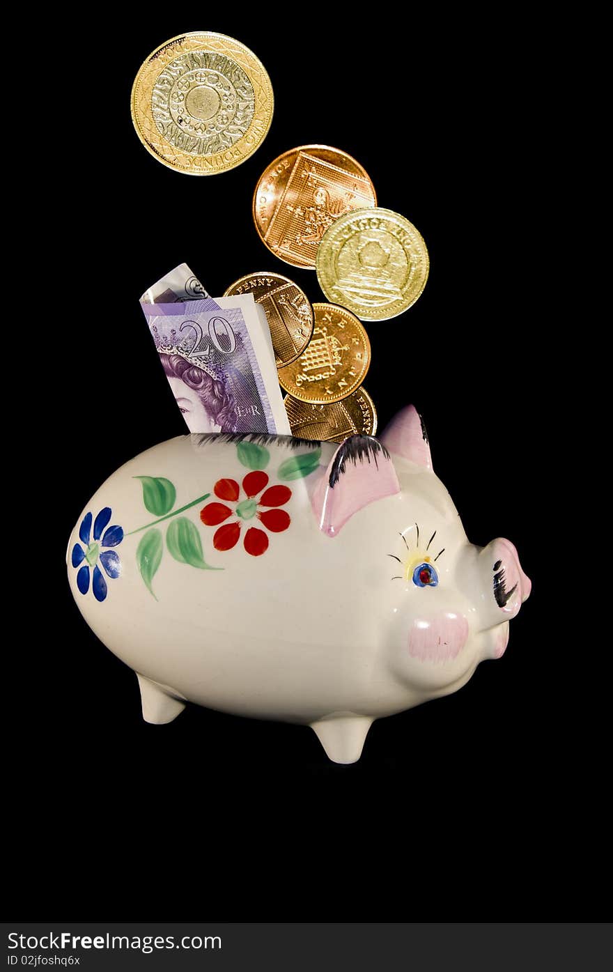 Old china piggy bank with flower pattern and money in the slot on a black background in portrait format. Old china piggy bank with flower pattern and money in the slot on a black background in portrait format