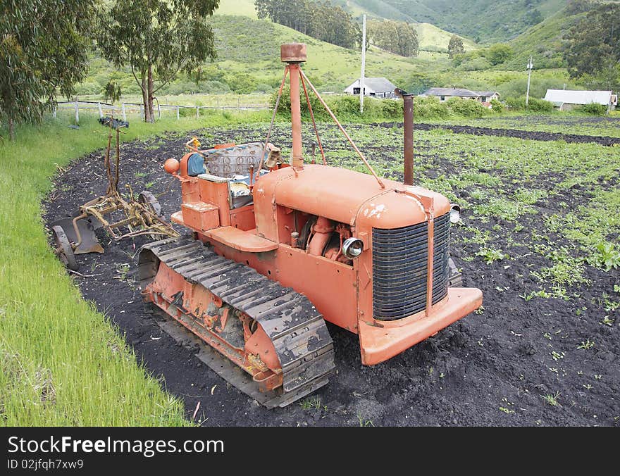 Tractor with springs exposed in the seat standing in a field with a tiller attached. Tractor with springs exposed in the seat standing in a field with a tiller attached