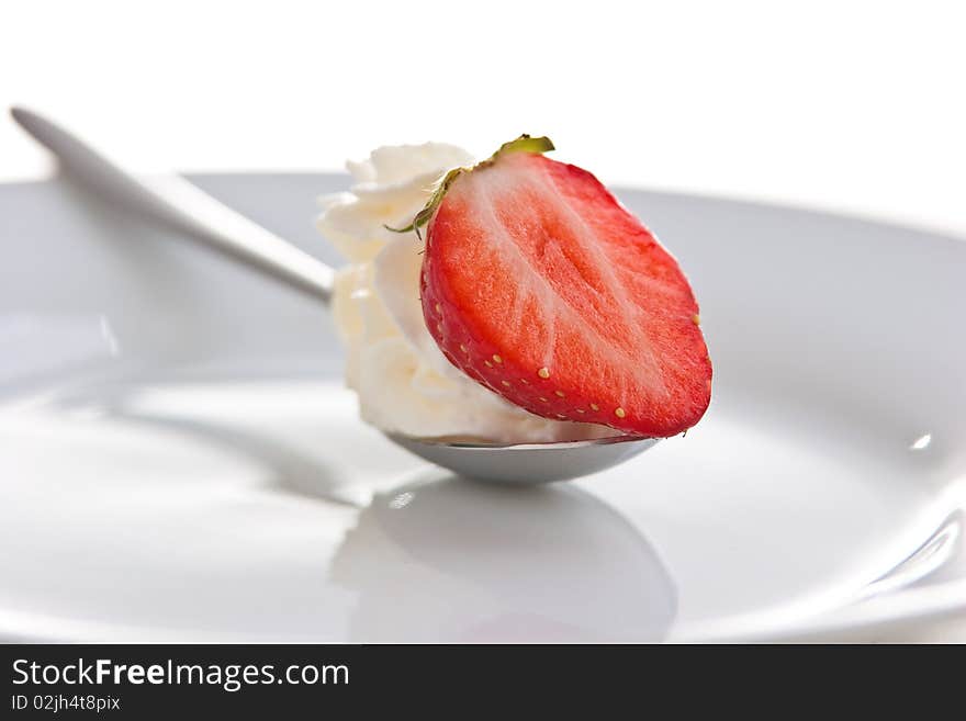 Single ripe fresh strawberry on spoon with cream isolated on white.