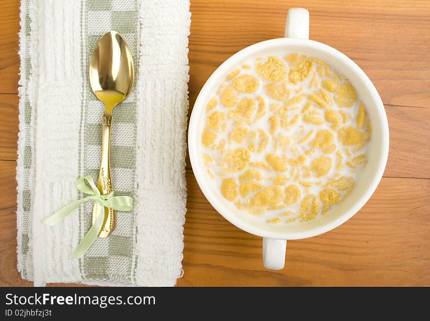 On the wooden table is breakfast cereal with milk, spoon and napkin