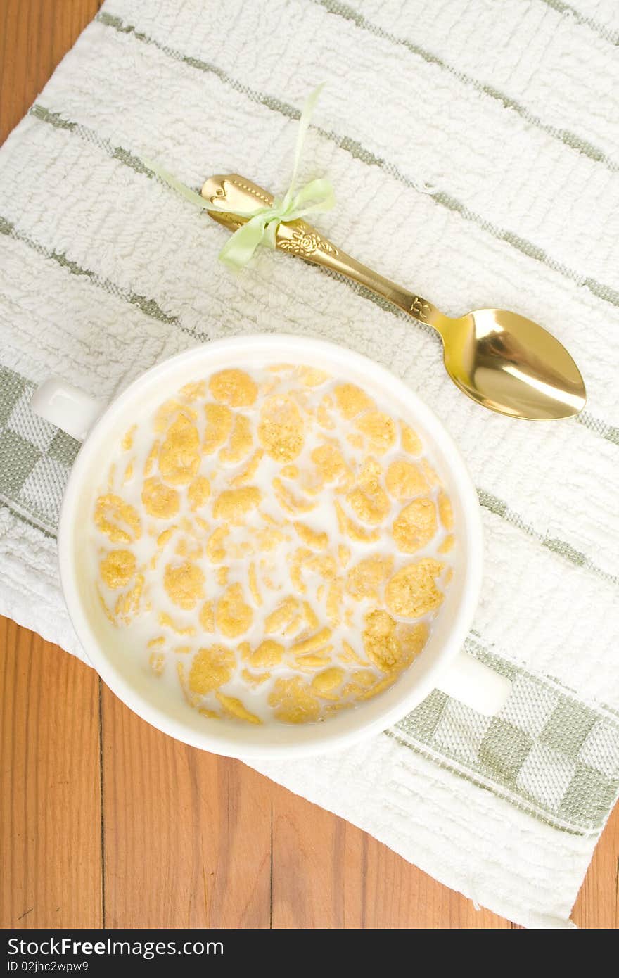 On the wooden table is breakfast cereal with milk, spoon and napkin