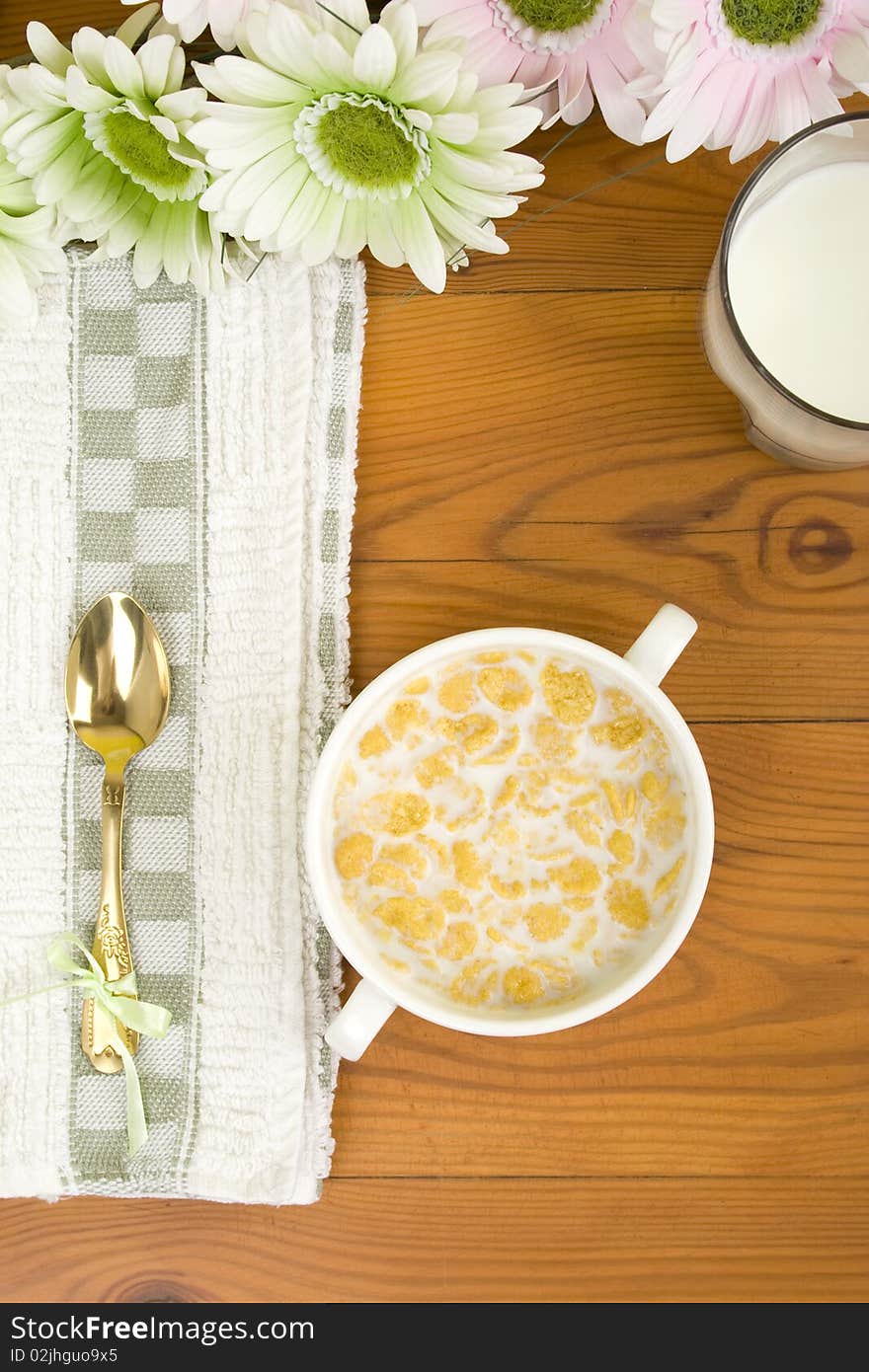 On the wooden table is breakfast cereal with milk, spoon and napkin