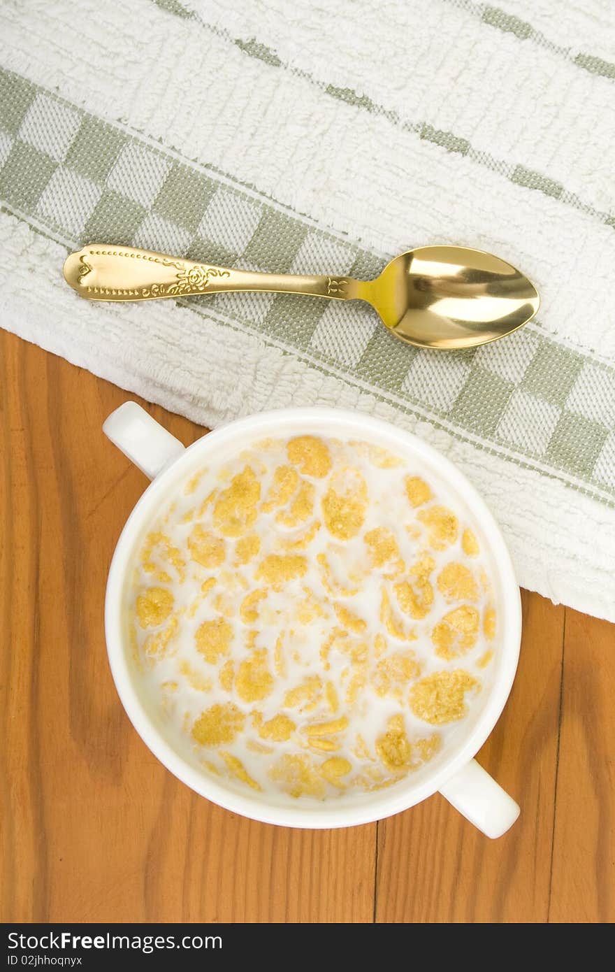 On the wooden table is breakfast cereal with milk, spoon and napkin