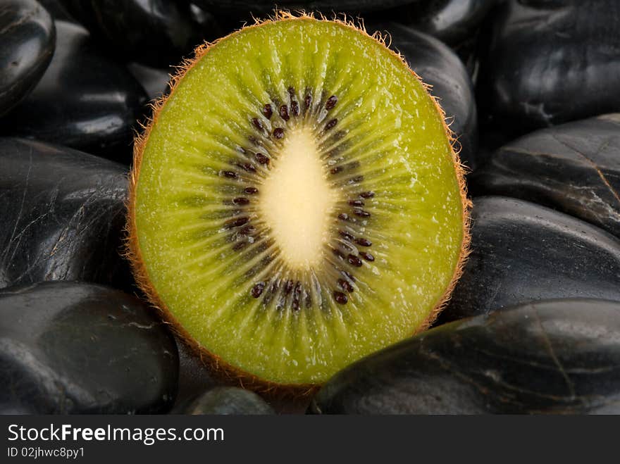 Half kiwi on dark stones close up