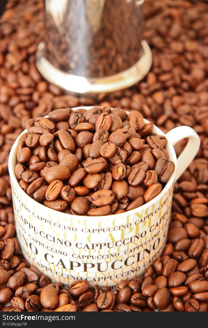 Fresh brown coffee beans in a cappuccino cup, metal coffee jar in the background