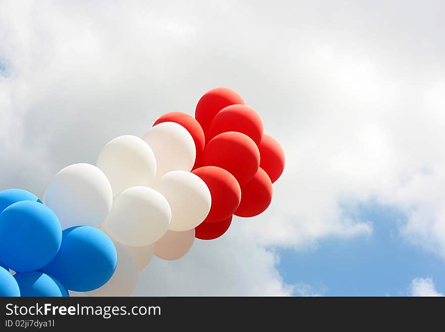 Garland of inflatable spheres of red, white and dark blue colour against the sky.