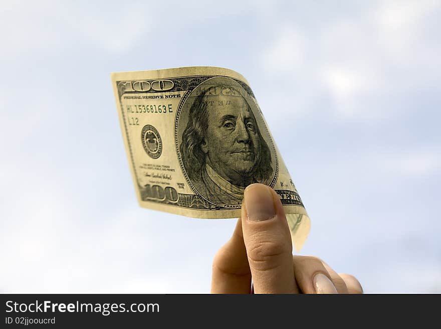 Hundred dollars in a female hand on a background of the light-blue sky. Hundred dollars in a female hand on a background of the light-blue sky