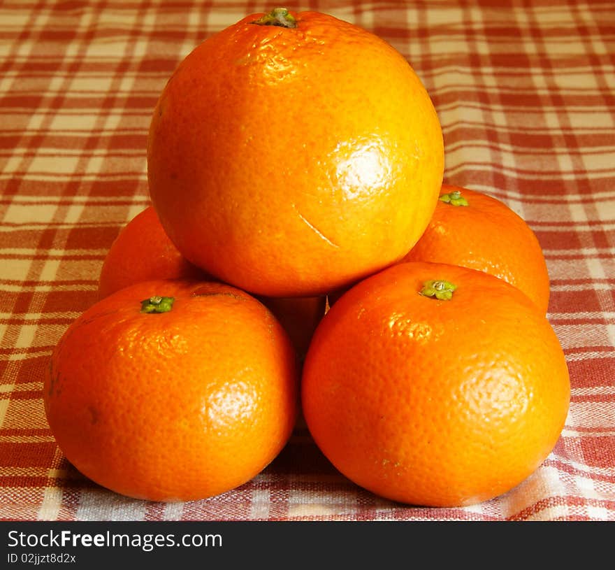 Pyramid of oranges and mandarins into a background with plaid tablecloth.