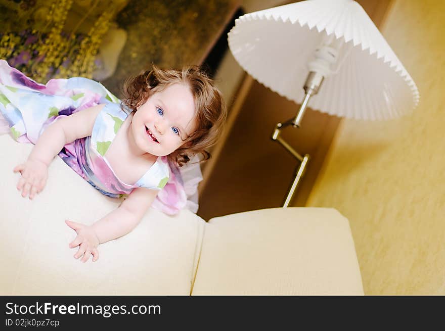 Baby-girl well-dressed lies on sofa near lampshade and smile. Baby-girl well-dressed lies on sofa near lampshade and smile