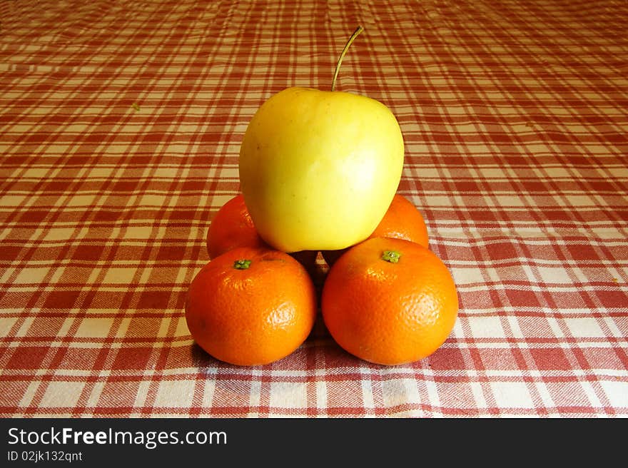 Pyramid of oranges and apple into a background with plaid tablecloth.
