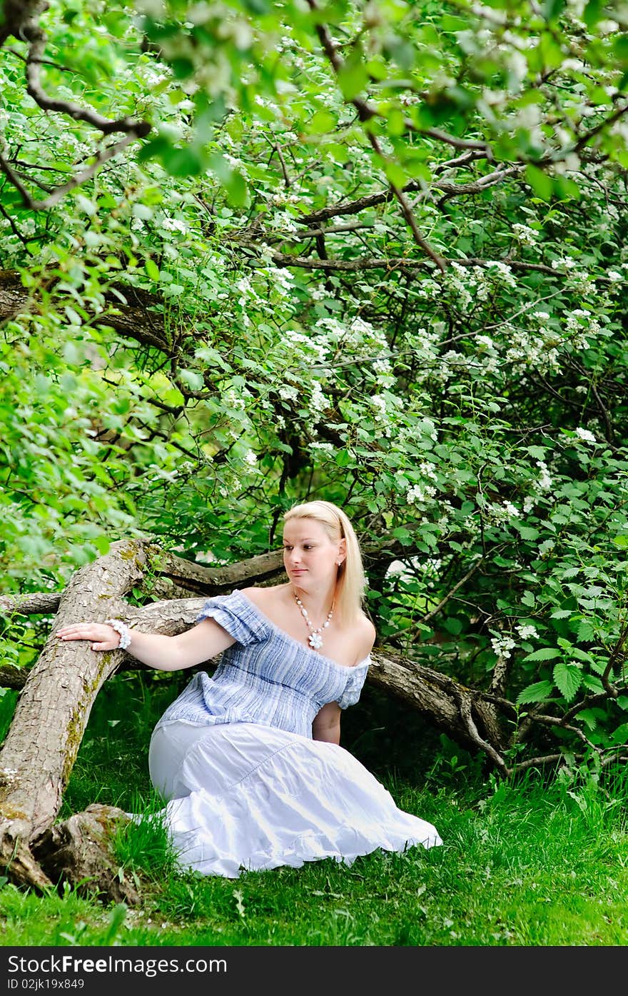 Beautiful pregnancy woman sits on the grass under the big blooming tree. Beautiful pregnancy woman sits on the grass under the big blooming tree