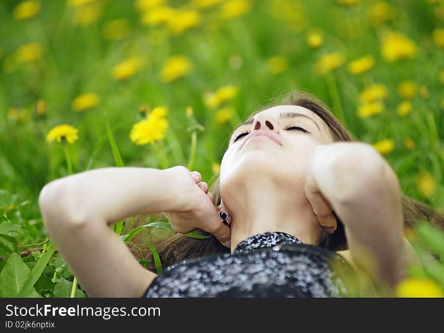 The girl lying in a green grass with yellow wild flowers