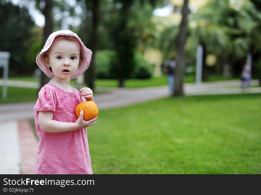 Adorable toddler girl holding a big orange