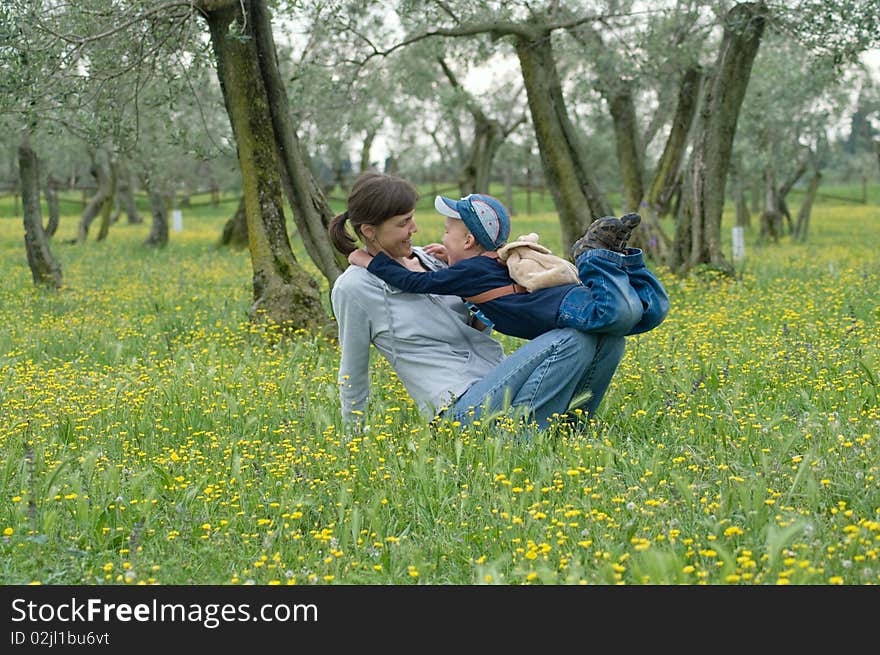 Mother and child playing in an olive grove in the meadow of dandelions. Mother and child playing in an olive grove in the meadow of dandelions.