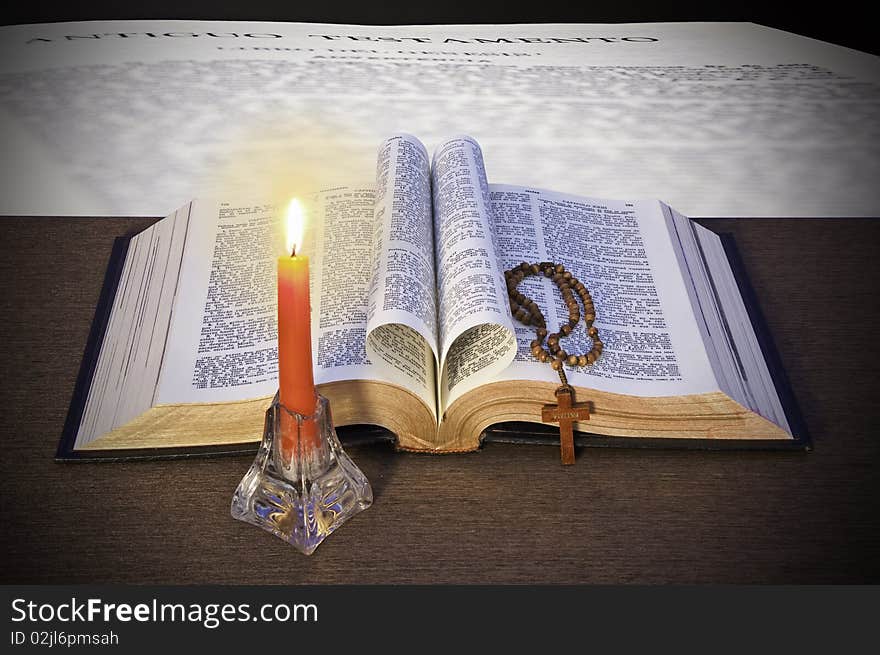 The Holy Bible, a rosary and a candle, on a background of a page of the Bible