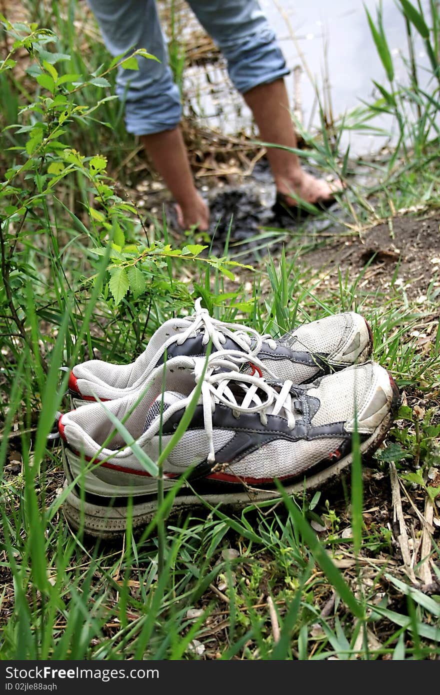 Masculine trainers stand on a green grass on the riverside, in the background feet of man. Masculine trainers stand on a green grass on the riverside, in the background feet of man