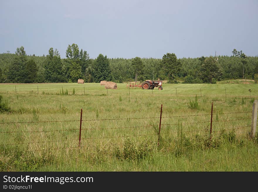 An old red tractor and a hay bale in a rural Alabama field. An old red tractor and a hay bale in a rural Alabama field.