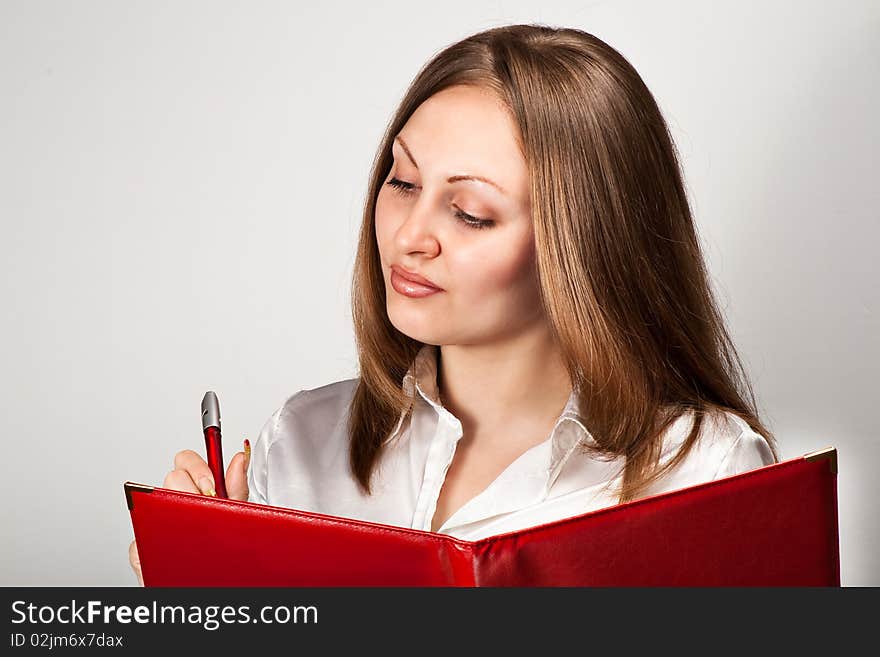 Pretty young woman writing in notice book over gray background