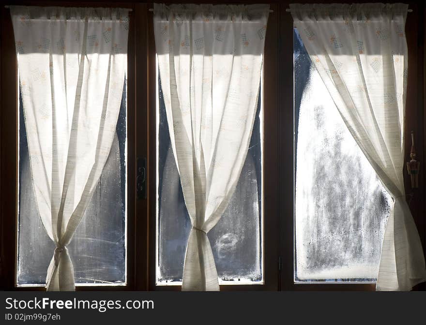 A window with curtains and cloudy glasses, in winter