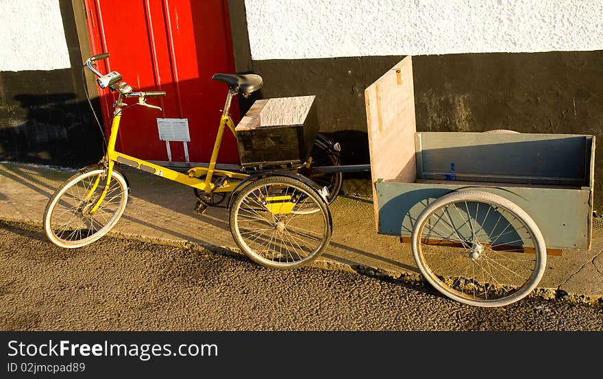 An image of a tricycle with trailer parked beside a red hotel door. An image of a tricycle with trailer parked beside a red hotel door.