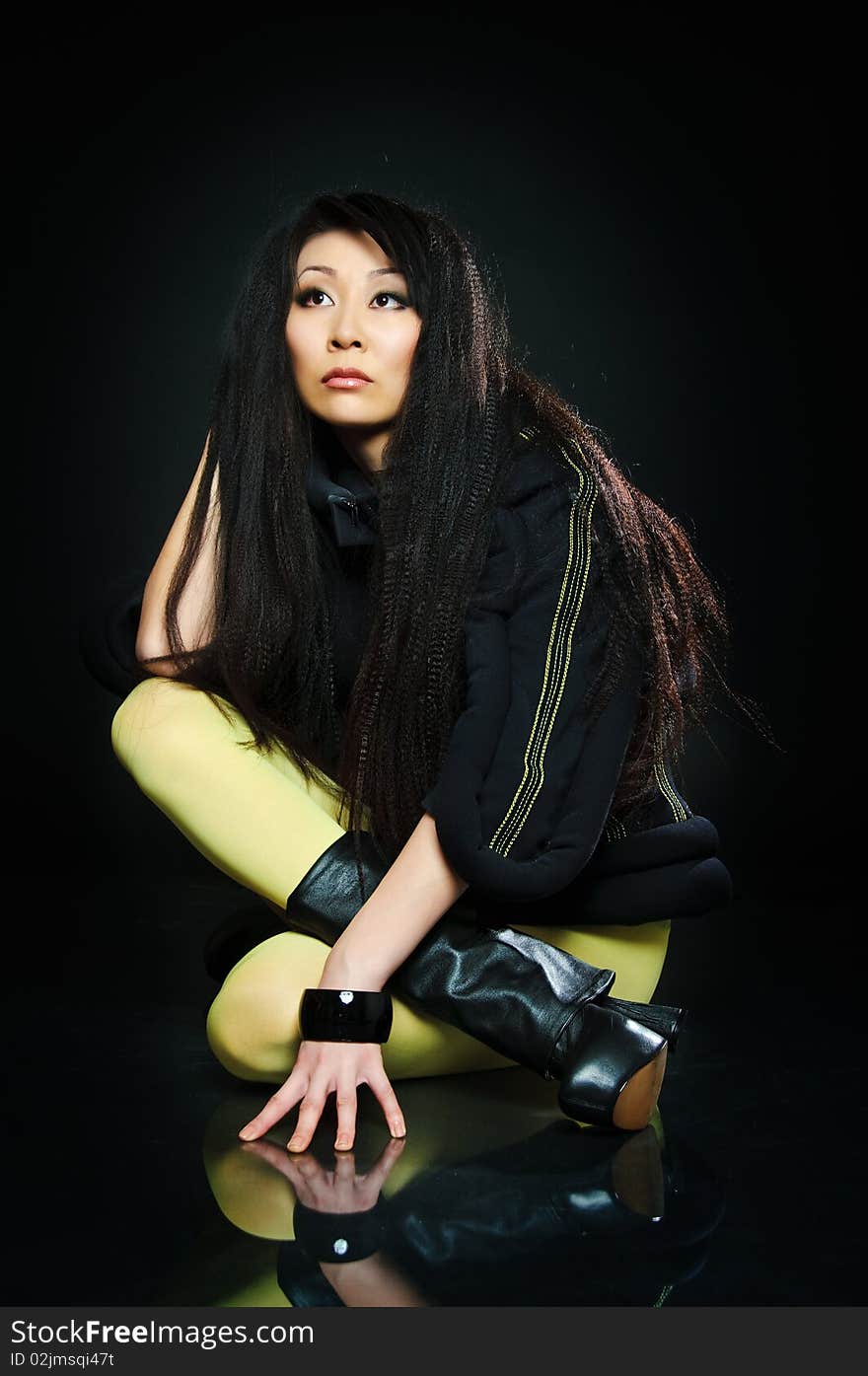 Sitting brunette asian model on black background with night reflections