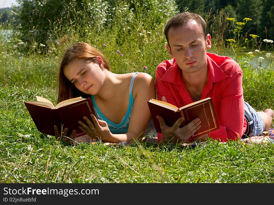 Young cople laying on a blanket on the grass on a hot summer day and reading book. Woman and man are enjoying the sunshine in a park. Just happy couple relaxing. Young cople laying on a blanket on the grass on a hot summer day and reading book. Woman and man are enjoying the sunshine in a park. Just happy couple relaxing.