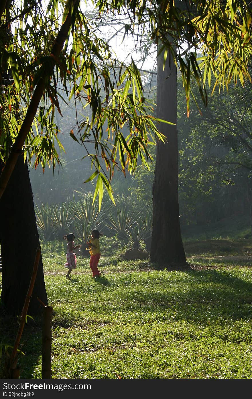 Two girls playing on grassy ground in the morning sunlight in a garden. Two girls playing on grassy ground in the morning sunlight in a garden