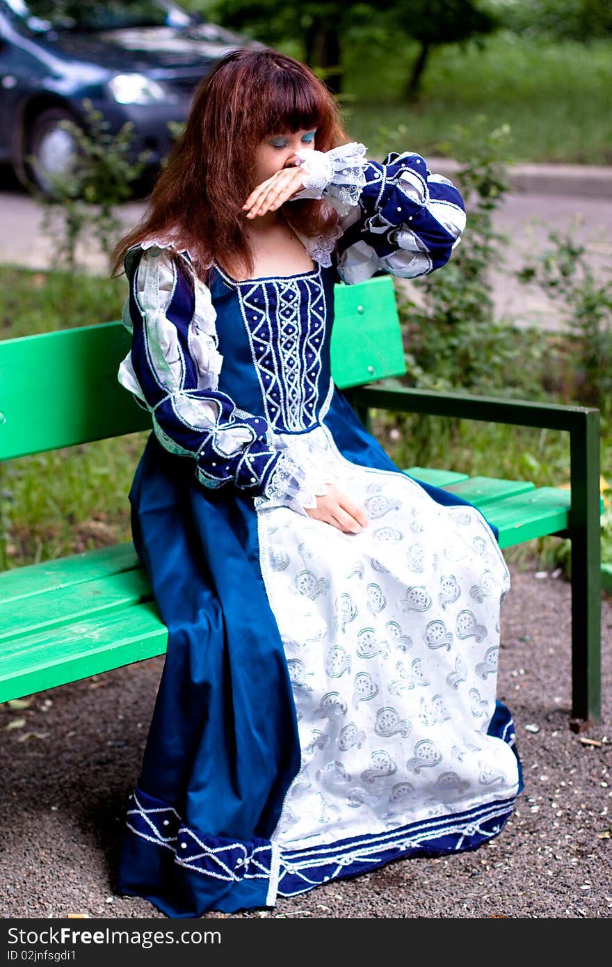 A girl in medieval blue dress sitting on a bench. A girl in medieval blue dress sitting on a bench