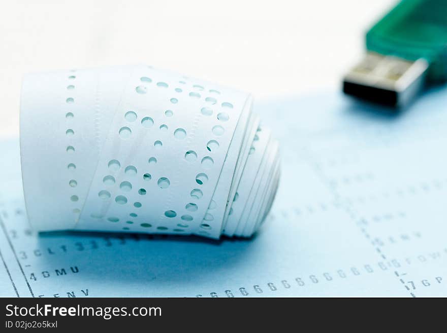 A role of computer punched paper tape with cards and usb stick showing old and new items of computing. A role of computer punched paper tape with cards and usb stick showing old and new items of computing.