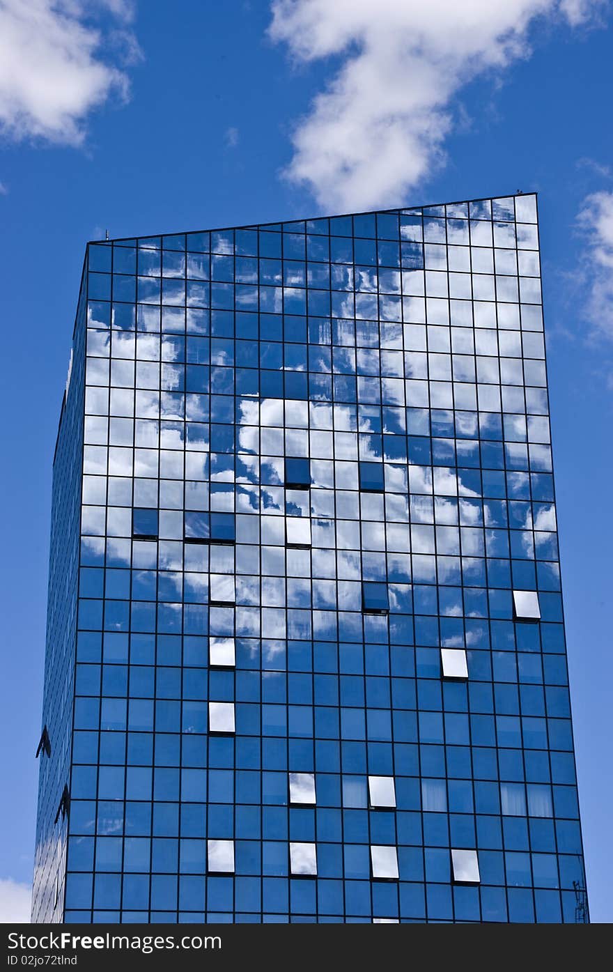 Glass tower with blue sky with clouds reflecting in the glass.