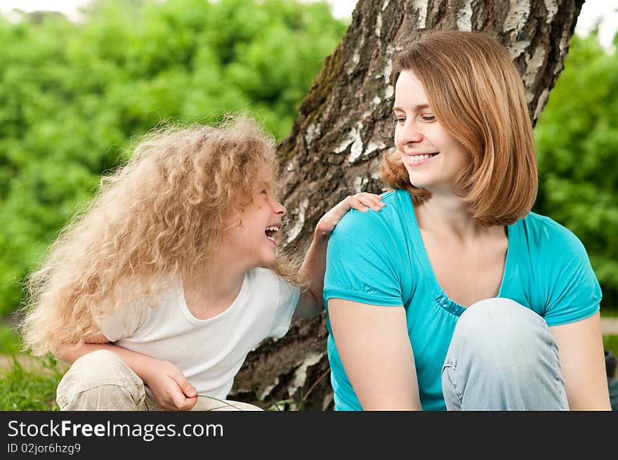 Happy young mother sitting in park with her beautiful laughing daughter. Happy young mother sitting in park with her beautiful laughing daughter