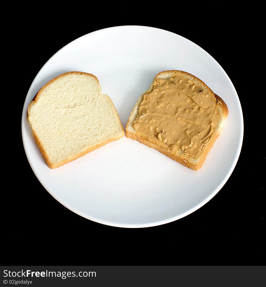 An open crunchy peanut butter sandwich made with white bread is on a white plate with black background